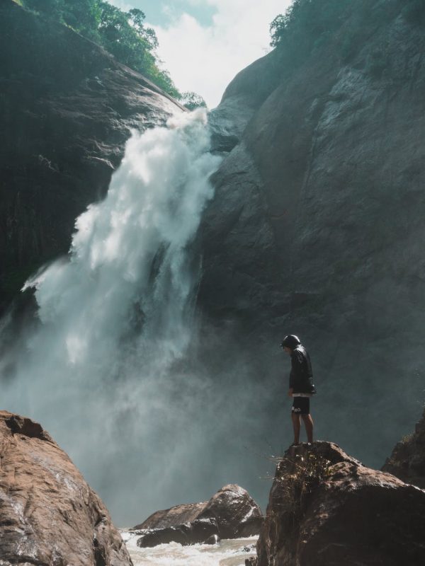 man standing on brown rock cliff in front of waterfalls photography